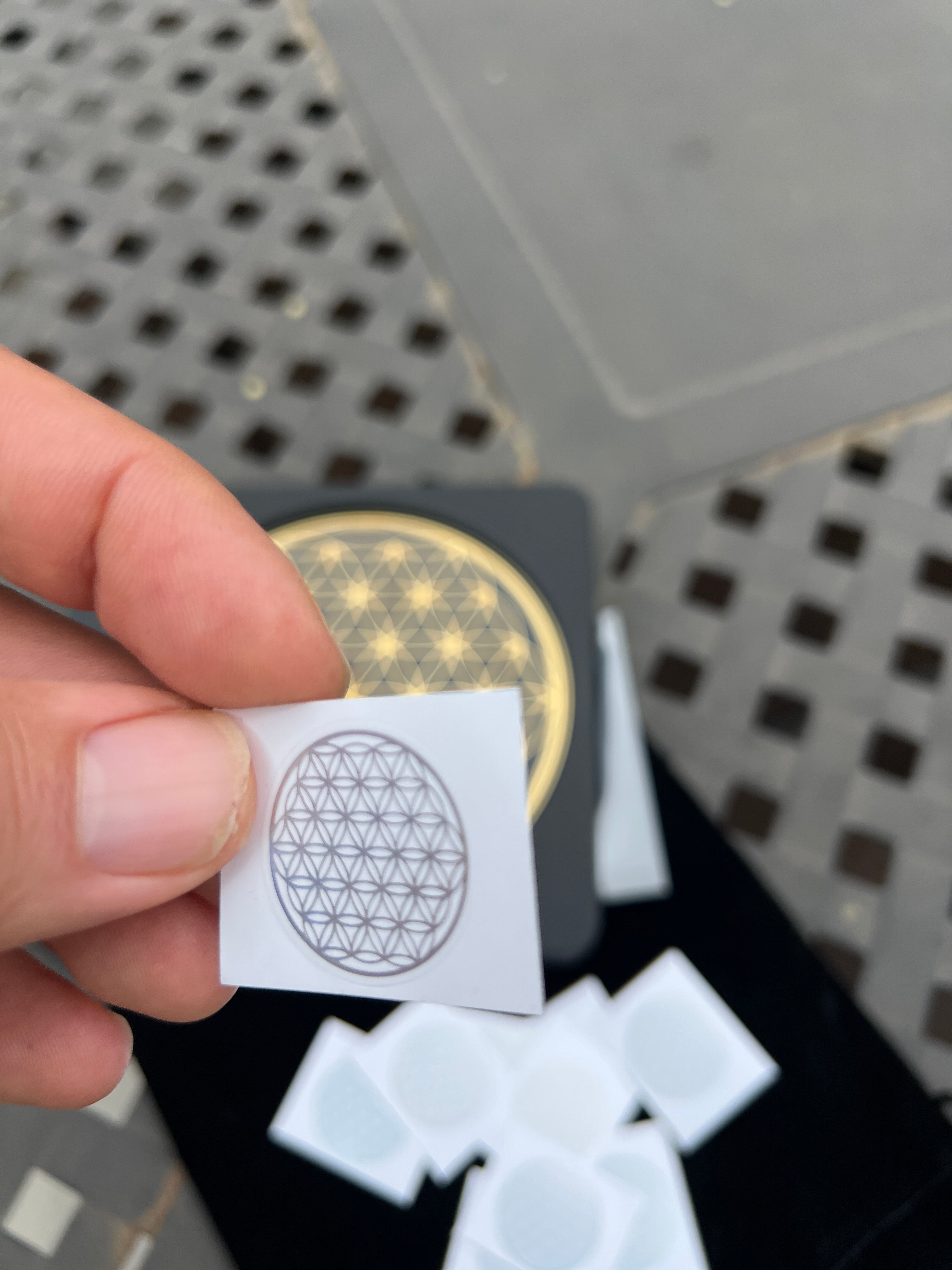 Hand holding Sacred Flower of Life patches with geometric design and multiple patches in background